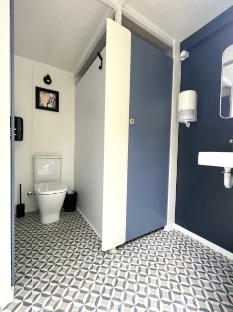 Aseos con un inodoro blanco, lavabo y paredes de colores azul y blanco. Suelo de baldosas.